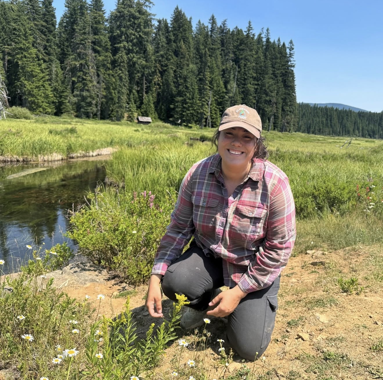 Makayla Hartness kneeling beside wildflowers along a creek